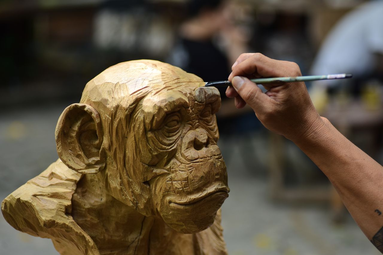 about-01 Close-up of an artist painting a carved wooden chimpanzee sculpture outdoors.