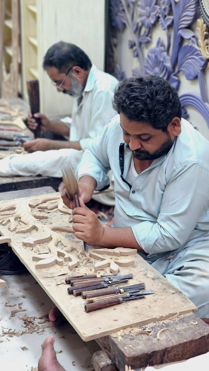 gallery-2 Artisans meticulously carving wood in a workshop, showcasing traditional craftsmanship.