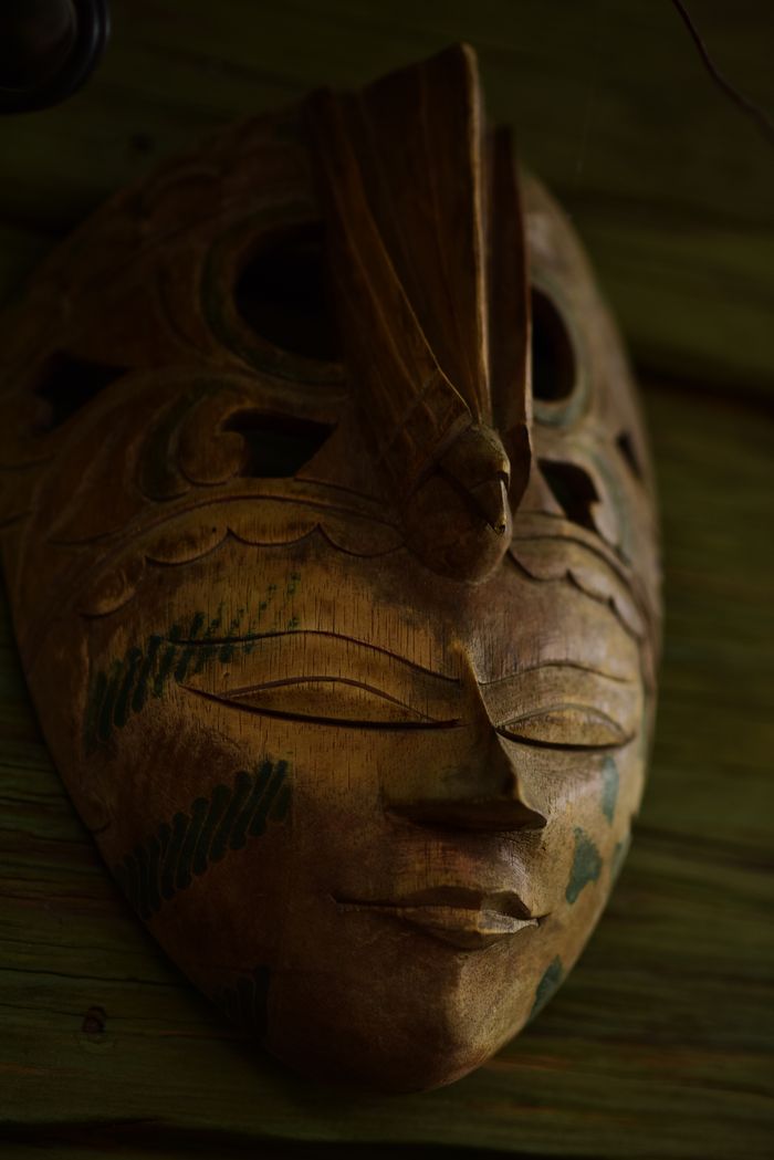 services-02 A detailed tribal wooden mask with green accents displayed on a rustic wooden wall.