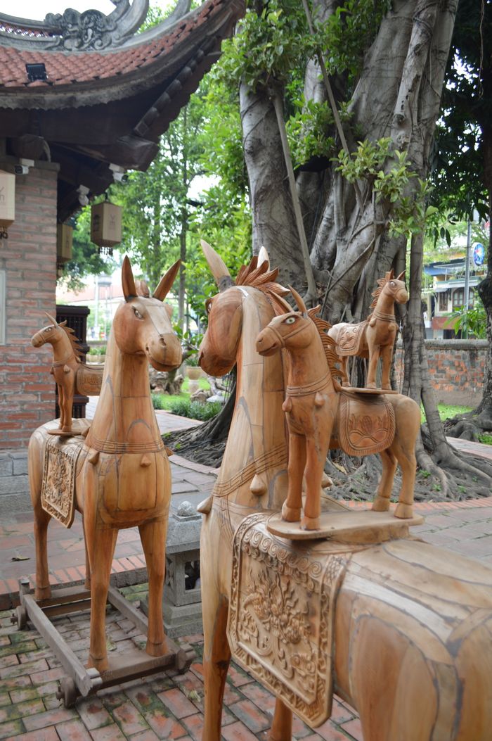 services-01 Intricate wooden horse sculptures displayed outdoors in a garden setting, showcasing cultural craftsmanship.